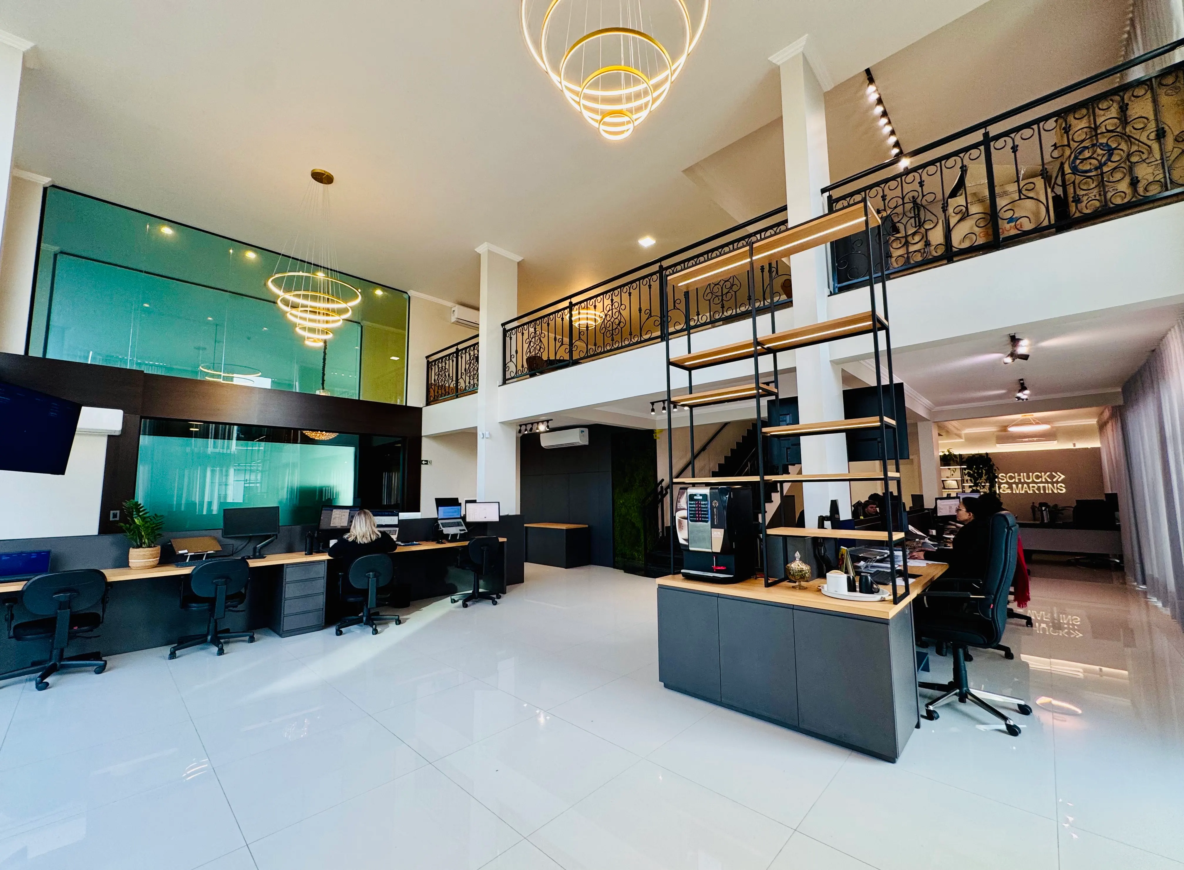 Interior da sede da Schuck & Martins com pé-direito duplo, mezanino e sala de reunião envidraçada